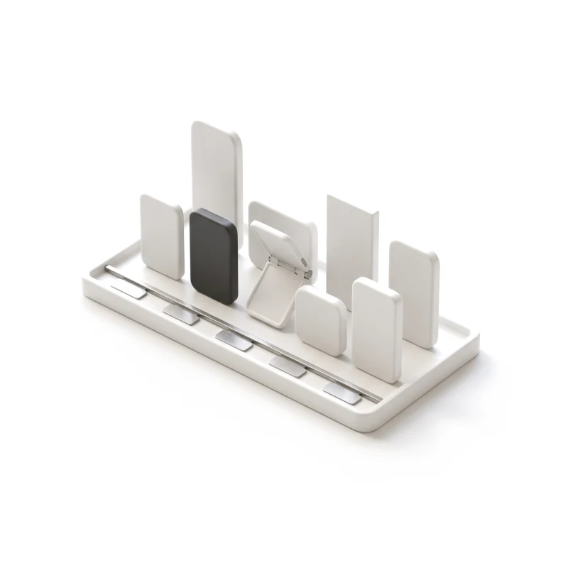 A shallow white ceramic tray holding a row of ceramic phone blanks of different sizes and shapes, one half-open folding phone, one in graphite, steel tags along the front.