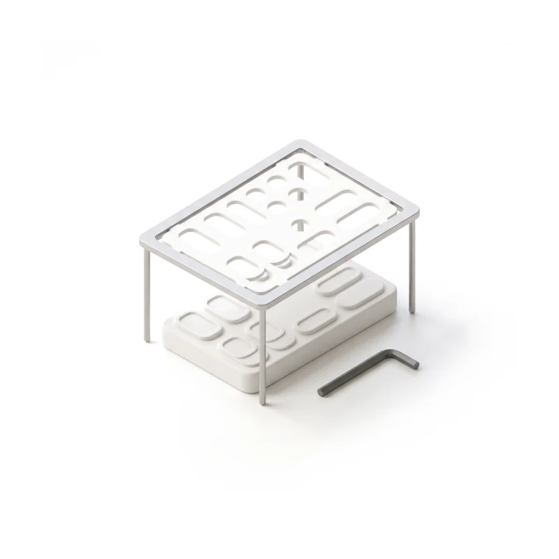 A ceramic stencil in a steel frame held over a white ceramic phone with the same raised layout, a steel hex key lying beside it.