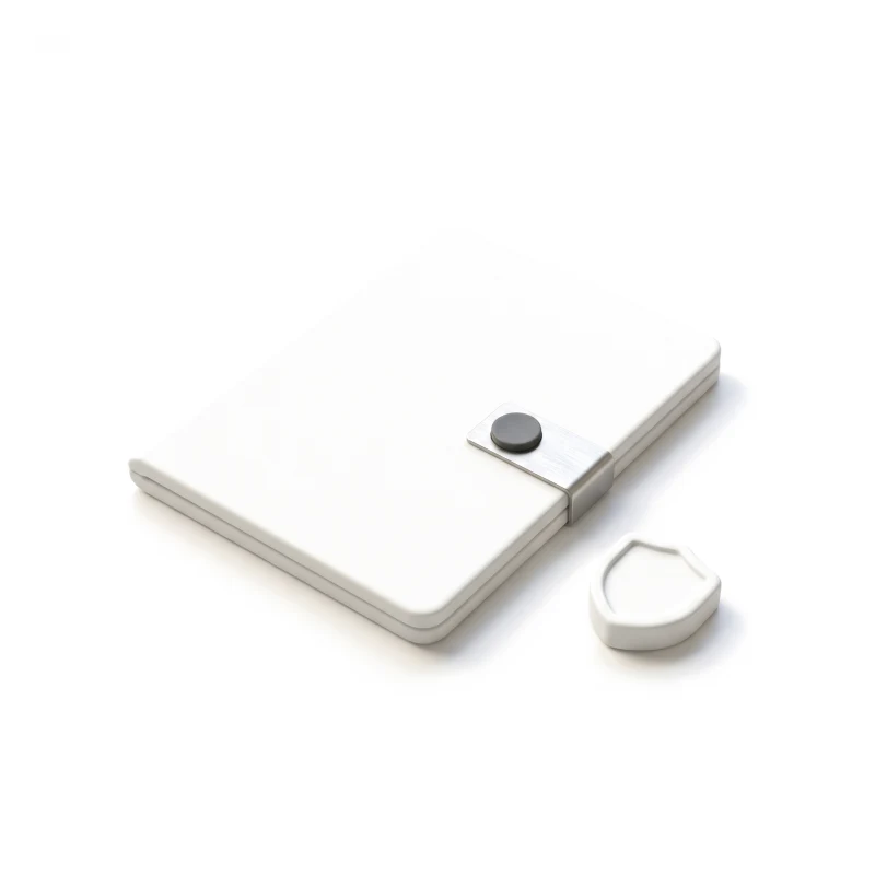 A closed white ceramic folder held by a steel clasp with a small graphite seal, a ceramic shield token beside it.