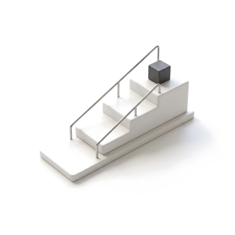 A ceramic base with three steps rising left to right, a thin steel rail running up them and a graphite cube on the top step.