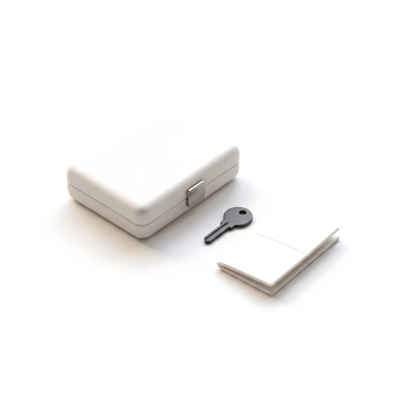 A closed ceramic case with a steel latch, a graphite key and a folded booklet beside it.