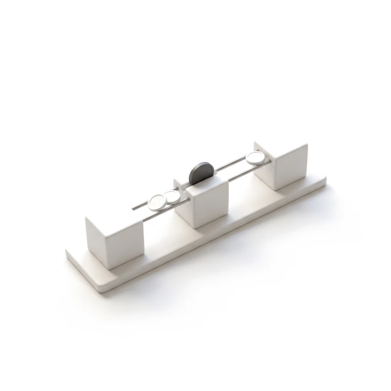 Three white ceramic blocks on one base, joined by steel rails that carry ceramic coins, a graphite coin in the middle block.