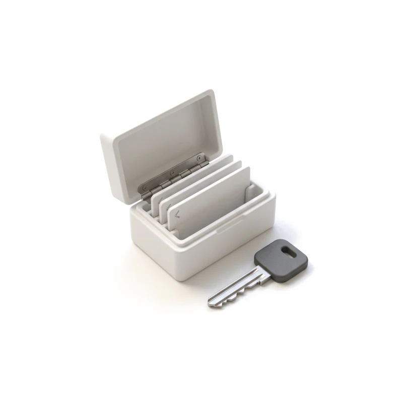 A small ceramic case with its lid half open over three ceramic plates carved with angle brackets, a steel key with a graphite head in front.