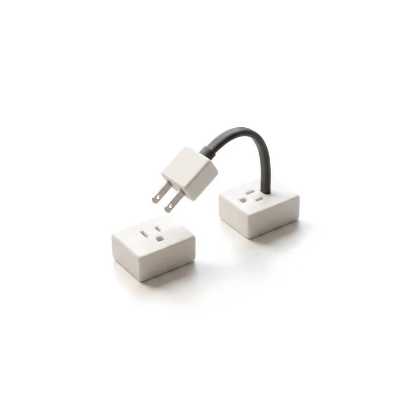 A ceramic plug with steel prongs lifted from one ceramic socket towards another, its short cable graphite.