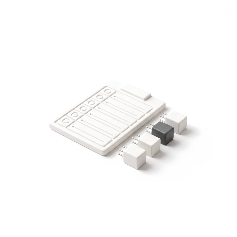 A flat ceramic board carved with a checklist of raised rows, a short row of ceramic plug-in modules with steel pins beside it, one module in graphite.