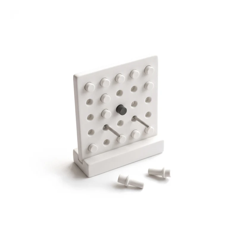 A ceramic pegboard of white pegs, two pulled out onto the ground and steel pieces fitted in their place, one peg graphite.